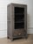 This character-rich wooden glass-front cabinet features a beautifully weathered gray-washed finish that enhances the...