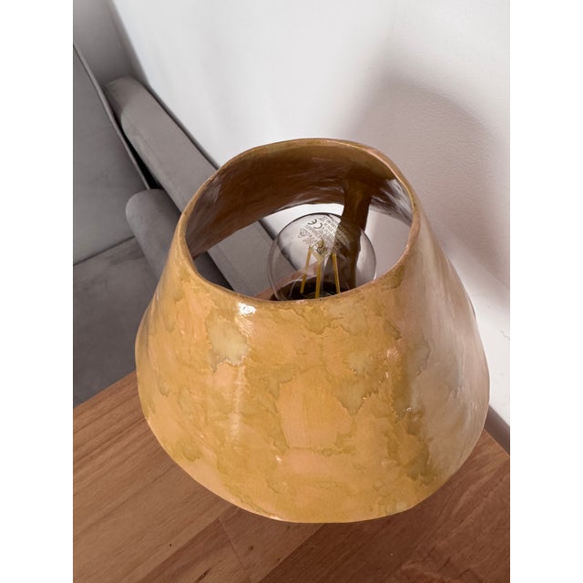This handmade ceramic table lamp is crafted from natural clay and finished with a ochre color glazed surface. The lamp is...