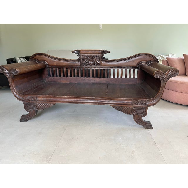 Hand-carved solid wood daybed with a dark brown finish. This piece has a slatted backrest and scrolled arms. The central...