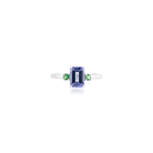 This refined, contemporary three-stone ring features an emerald-cut center tanzanite flanked by round-cut tsavorites,...