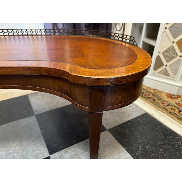 Interesting Antique coffee table. Kidney shaped with a 1" tall brass gallery half way around. Simple leg. Lighter wood...