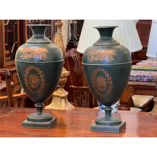 A handsome pair of tole urns in deep green with gilt decoration in the Neoclassical taste. Each urn has a classical ovoid...
