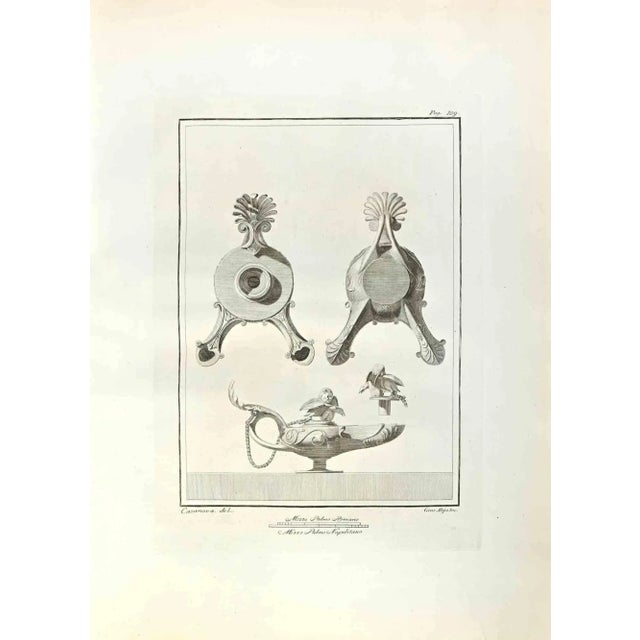 Oil Lamps with Cupid from "Antiquities of Herculaneum" is an etching on paper realized by Giuseppe Aloja in the 18th...
