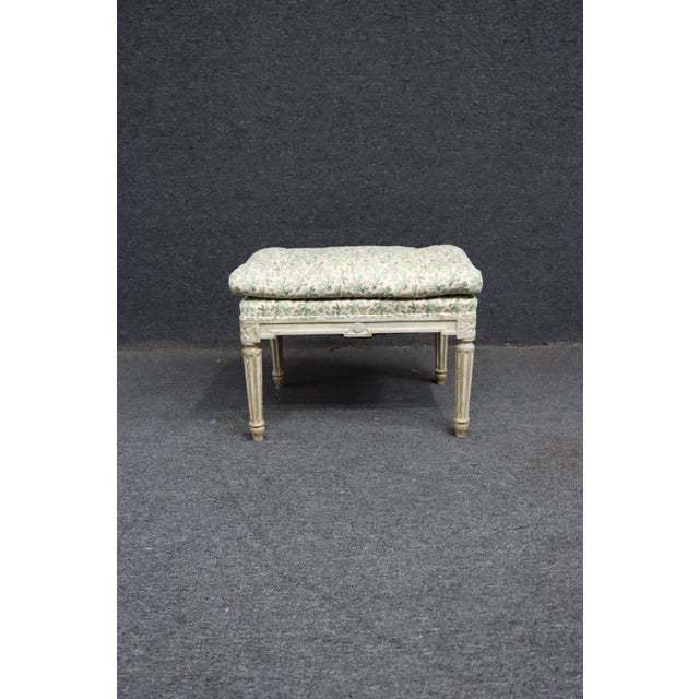 Small upholstered footstool with a carved wood frame in a Louis XVI style. Features fluted legs, carved corner details,...