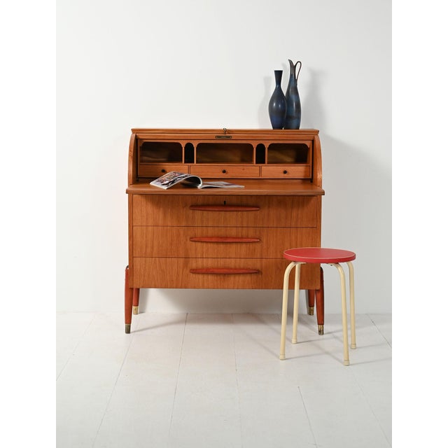 Scandinavian teak secretary with roller shutter, reddish wooden handles and legs with brass tips. Original manufacturer's...