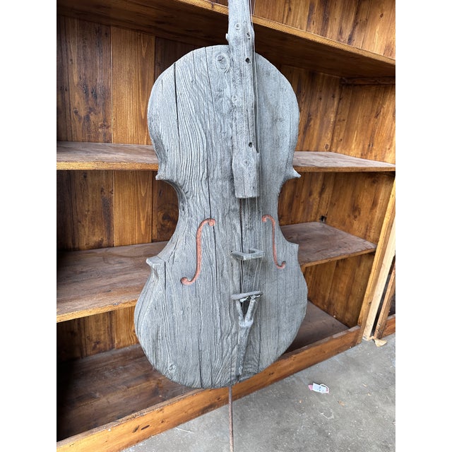 A striking large-scale hand-carved wooden sculpture in the form of a cello, blending rustic craftsmanship with sculptural...