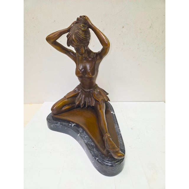 This bronze statue captures the delicate beauty of a ballerina seated gracefully as she adjusts the bun atop her head....