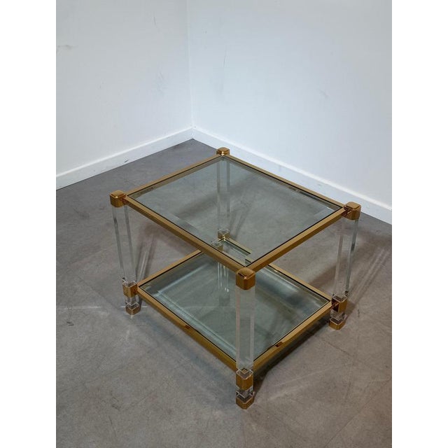 Elegant vintage side table combining clear acrylic glass legs with polished brass frames and corner fittings. A classic...