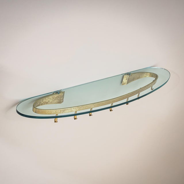 Wall-mounted coat rack model 2185 featuring an oval shelf of blue-tinted glass. The brass mounting incorporates sliding...
