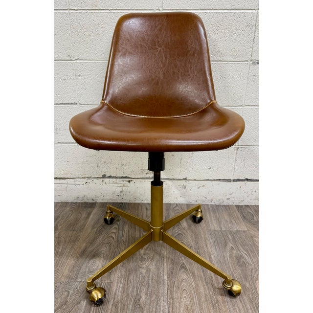 This is a stylish World Market Marina office chair featuring rich cognac brown faux leather upholstery, a brushed brass...