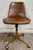 This is a stylish World Market Marina office chair featuring rich cognac brown faux leather upholstery, a brushed brass...