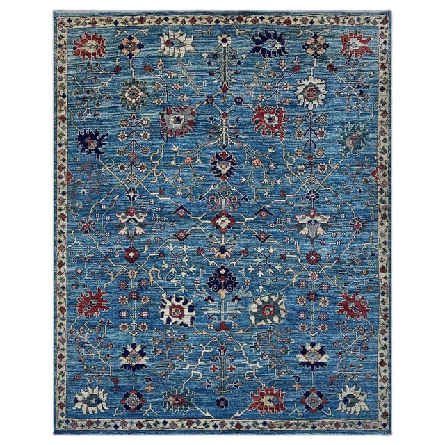 A rich cornflower blue Oushak area rug, its field laid out as a network of fine ivory and gold branches, each one blooming...