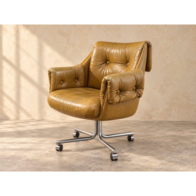 Low and round-backed, this pair of mid-century modern swivel chairs is upholstered in a tan leather look with button...