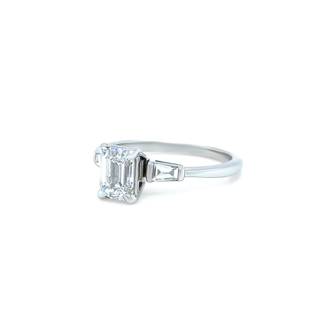 A refined emerald cut diamond ring crafted in 14ct white gold, featuring a striking centre diamond accented by tapered...