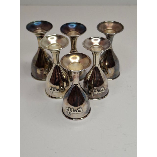 This charming set consists of six miniature sterling silver kiddush cups (small goblets), each elegantly engraved with the...