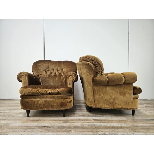 An elegant pair of vintage armchairs with a soft, enveloping design, featuring rounded armrests, a tufted backrest, and...