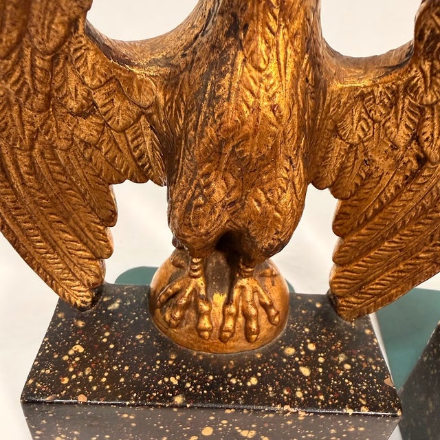 Vintage eagle bookends feature a striking gold-tone finish with detailed feathering, perched atop black speckled bases....