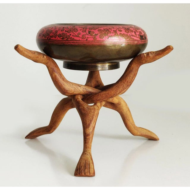 Hand carved interlocking and collapsible legs hold a sturdy brass bowl with pink lacquer details. The base of each leg is...