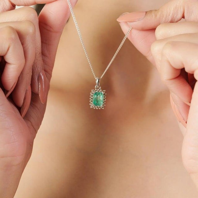 This pendant is crafted in 925 sterling silver and showcases a captivating 6.4 carat octagon-cut emerald at its center....