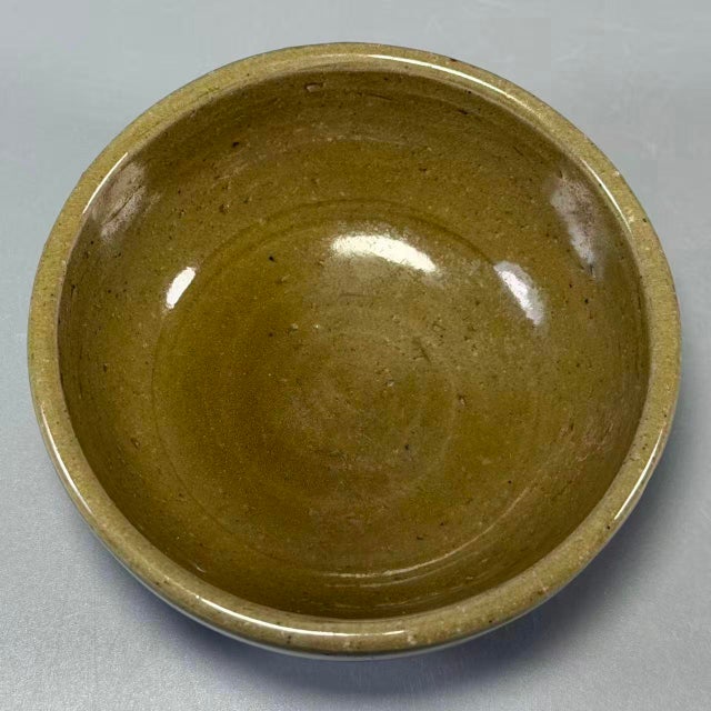 This compact ceramic bowl has warm olive‑brown glazed surface with subtle texture. The base is neatly finished. It is...
