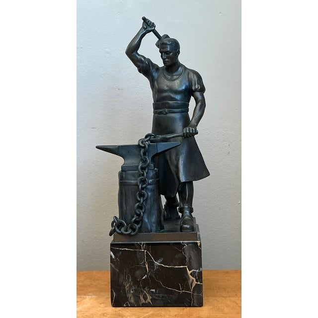 A striking bronze sculpture capturing a blacksmith mid-motion, hammer raised above an anvil in a scene charged with...