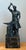A striking bronze sculpture capturing a blacksmith mid-motion, hammer raised above an anvil in a scene charged with...