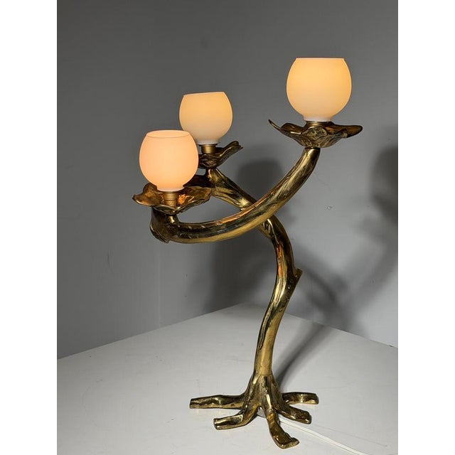 Distinctive bronze table lamp featuring an organic, tree-inspired design. A twisting stem rises from a root-shaped base,...