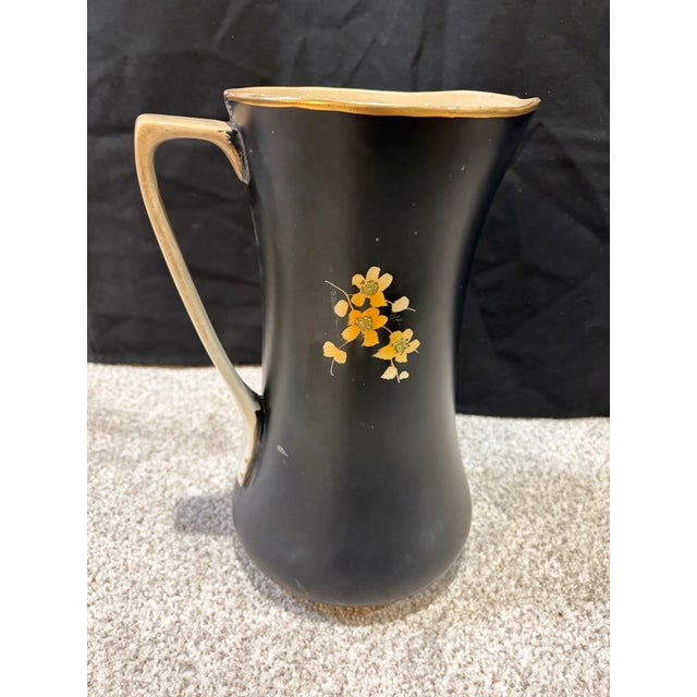 This is a vintage hand-painted ceramic pitcher featuring a matte black finish, red fruit illustrations and gold trim along...