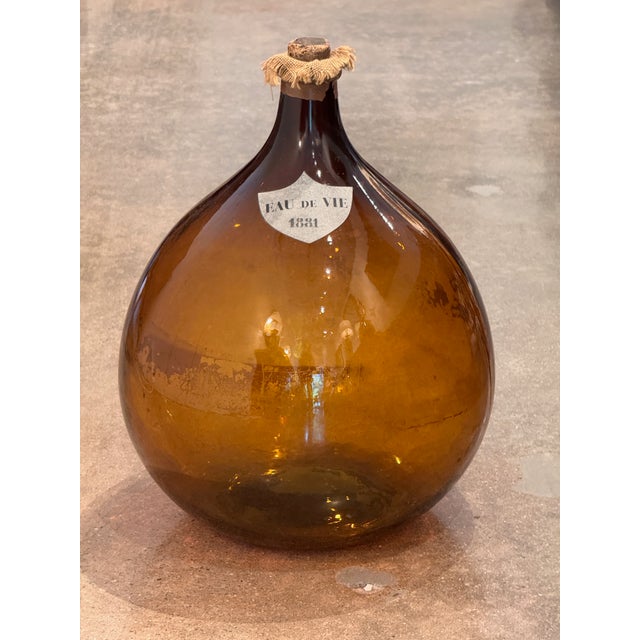 A blown amber glass demijohn with a shield reading "Eau de Vie 1881." Cork stopper with burlap collar.