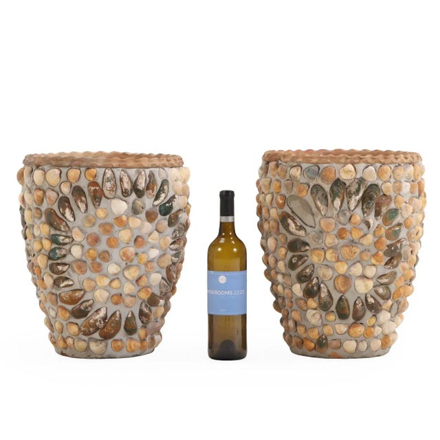 A decorative pair of concrete planters, each adorned with an intricate surface of applied shells in varied natural tones...