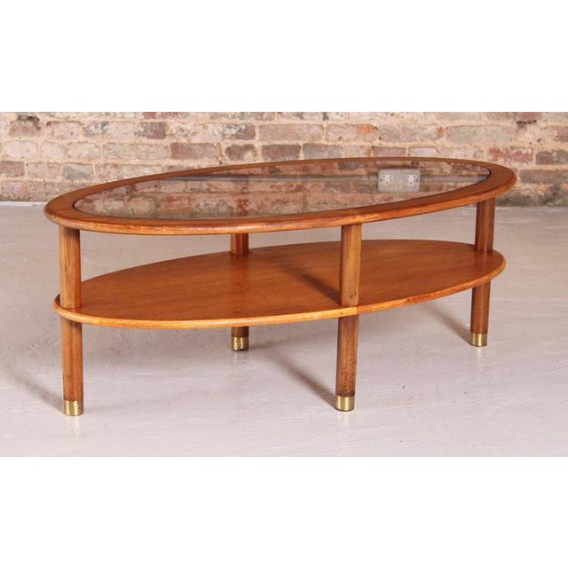 Mid Century oval 2-tier teak coffee table with a smoked glass top and brass feet by G-plan, circa 1970s. The table has...