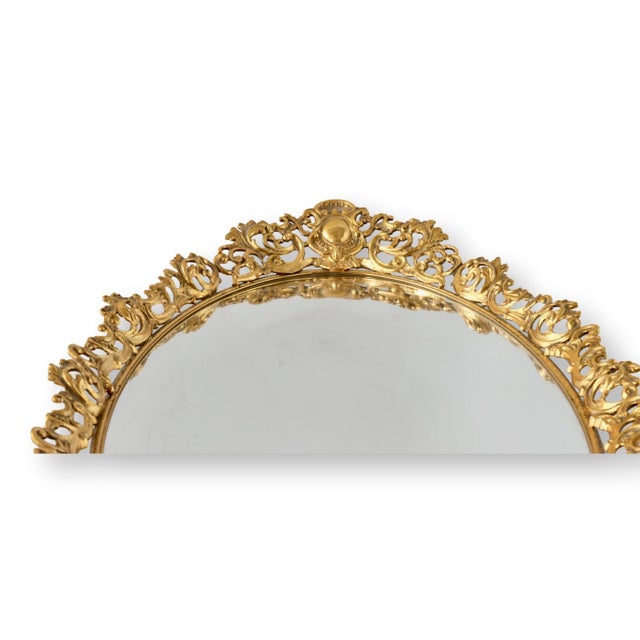 Heavy midcentury American vanity mirror with ornate gold filigree surround and elegant oval form. The richly detailed...