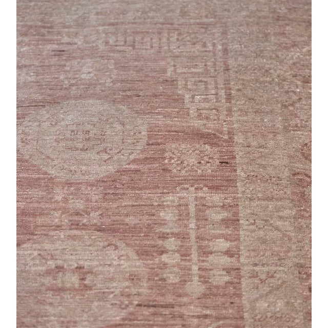 This revival Khotan rug has a dusty-rose field with a century column of three ivory roundels flanked by two columns of 5...