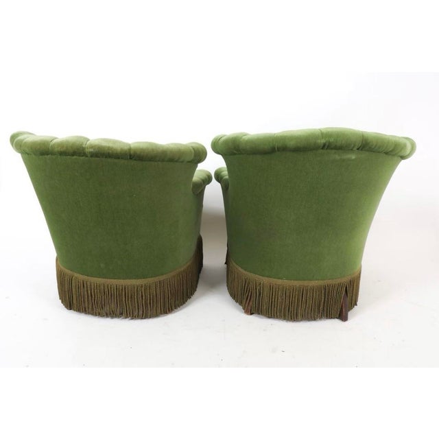 Luxurious pair of mossy green his and hers tufted velvet club chairs with scalloped backs, rolled arms, and full fringe...
