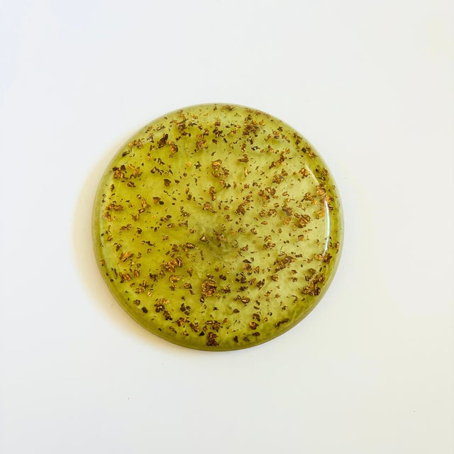A mid century circular green lucite trivet. Lovely gold flecks embedded in the lucite throughout. Slightly elevated on 3...