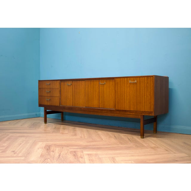 A mid-century sideboard by g plan (e. Gomme), dating to the 1960s, in a warm tola wood finish. the layout includes three...
