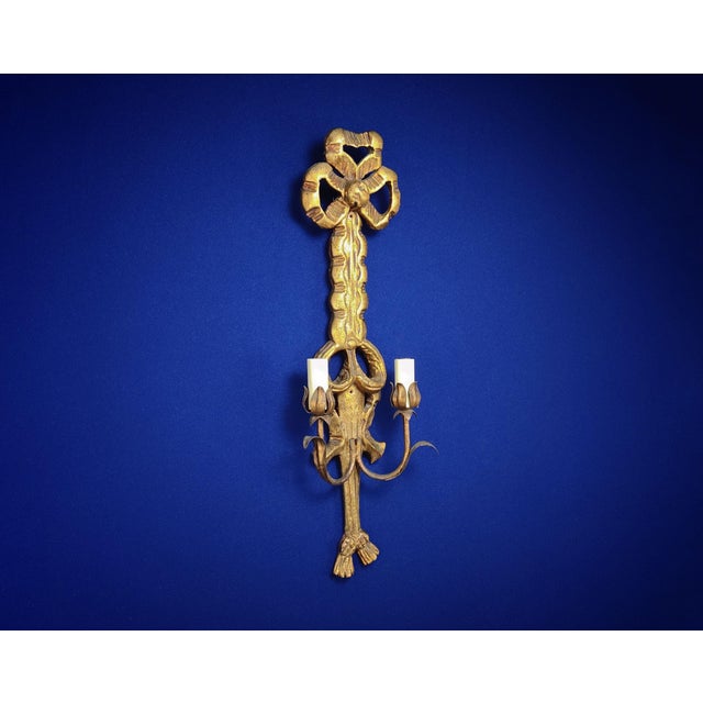 A very tall two-light ‘bras de lumière’ sconce executed in hand-carved and faux-distressed gilded wood decorated with bows...