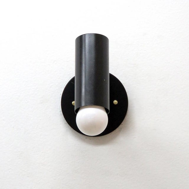 Elegant articulate wall lights, in black enameled metal with brass accents, swivel joint at the cylinder, complementary...