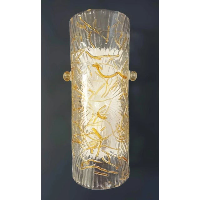 Italian wall light with a cylinder Murano glass shade in clear color with amber and gold texture, mounted on white metal...