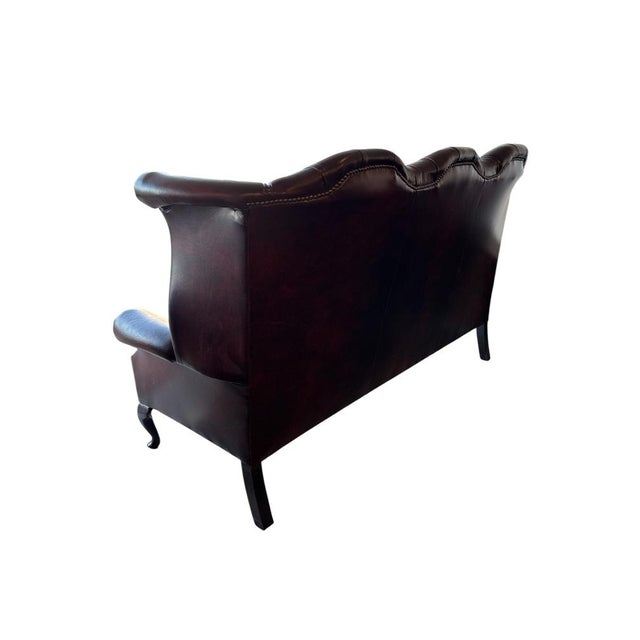 English high-back Chesterfield sofa in burgundy leather with deep button tufting, rolled arms, and nailhead trim. Raised...