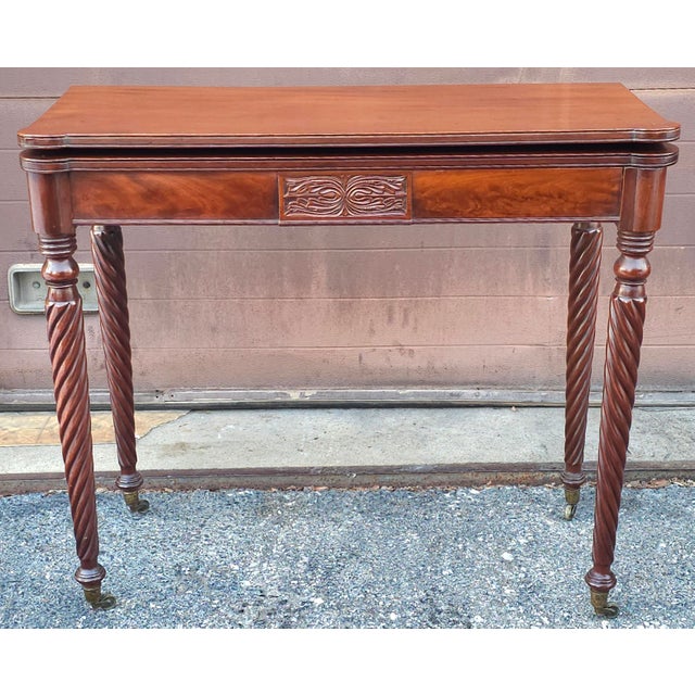 This is an antique Sheraton style mahogany flip-top game table, Circa 1800s It features a rectangular top with a molded...