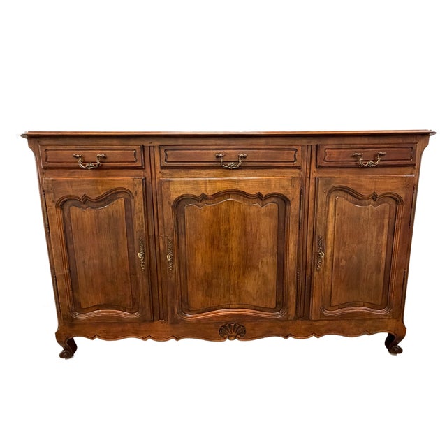 This is a charming French Provincial buffet features a warm walnut finish, shaped paneled doors, and classic Louis XV-...