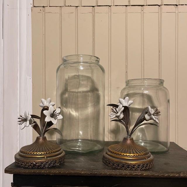 A set of 2 graduated canisters of clear glass with gold metal lids featuring a Reticulated edge and topped with white...