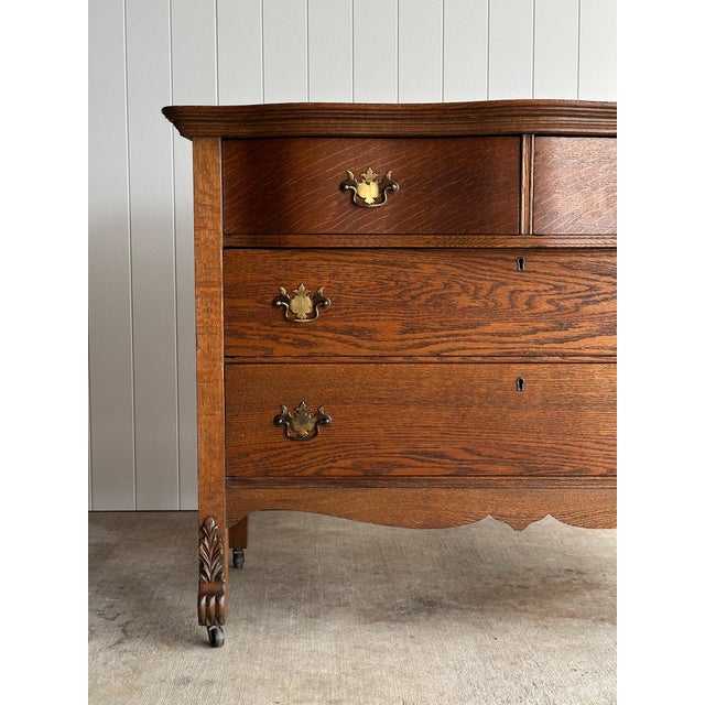 An antique oak chest of drawers featuring serpentine drawer fronts, original brass hardware, carved foliate feet, paneled...