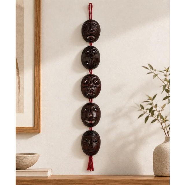A striking vintage Korean wall hanging composed of five miniature carved wooden character masks suspended vertically on...