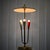 A modernist table lamp crafted from brass, featuring three arms set on a circular base. Each arm holds a conical...