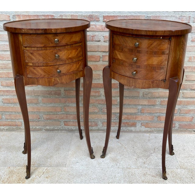 Elegant pair of French bedside tables in the Louis XV style, featuring oval tops decorated with delicate floral marquetry...