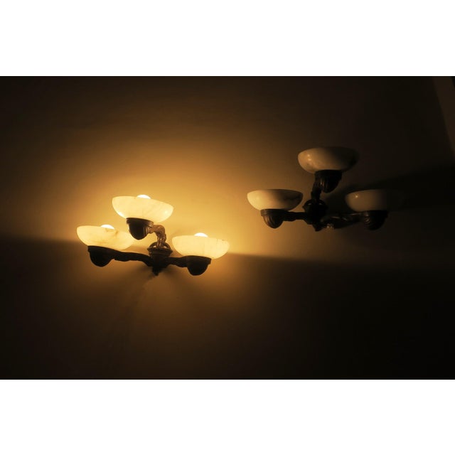 Antique pair of 3-light wall lamps in bronze with alabaster shades. Up to 250V (Europe/UK Standard).The wiring of this...