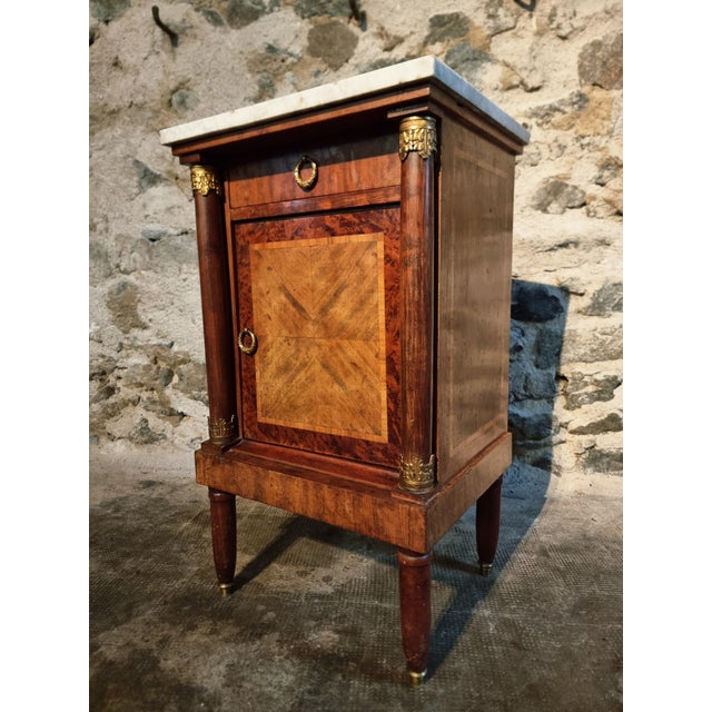 Refined French Empire bedside cabinet, crafted from walnut veneer, mahogany, and acajou wood. This elegant piece reflects...