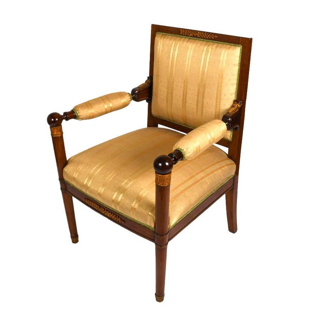 This antique French Empire-style chair offers a refined interpretation of the neoclassical elegance associated with the...